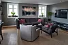 Moderne stue med sofaer, lenestoler, TV, planter og stort kunstverk på veggen.