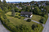 Et enebolig med stor gressplen i et grønt boligområde med trær, veier og hus i bakgrunnen.