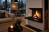 Moderne stue med tent peis, sofa, salongbord og spisebord foran store vinduer.
